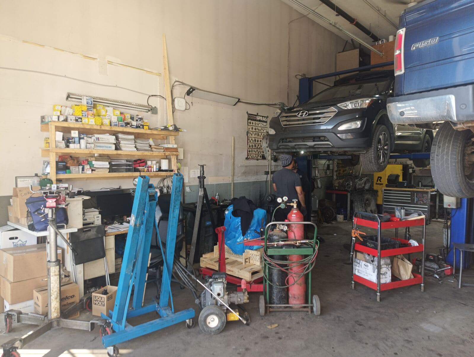Shop floor with engine hoist, parts shelving and a vehicle on the lift